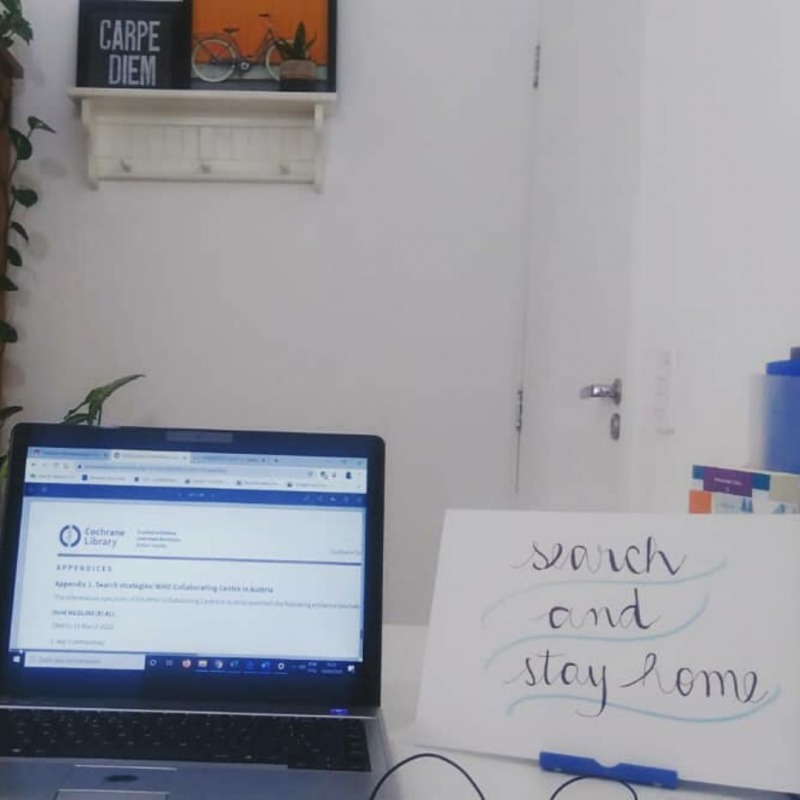 Picture of a computer on a table next to a sign that says "Search and stay home".