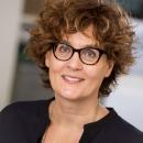 Anne Schilder, a white woman with black-framed glasses and short curly hair, smiles at the camera
