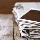 a stack of newspapers with a tablet