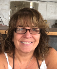 Eva Madrid, a woman with curly brown hair wearing rectangular glasses, looks at the camera and smiles