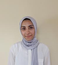 Sarah Tanveer, a woman wearing a lilac headscarf and white blouse, looks at the camera