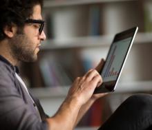 A man with curly hair and glasses looks at a graph on a tablet