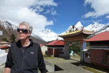 Jim Neilson, a white man with short white hair, stands in front of mountains and an ornate gate with sunglasses on