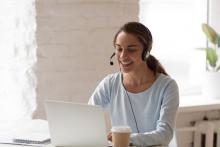 A woman wearing a headset smiles at her computer