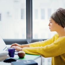 A woman with a head scarf and a yellow sweater works on a computer
