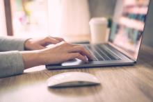 hands typing on a laptop computer, which is on a table next to a coffee and mouse