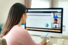 A woman looks at a computer with graphs and three other people on a conference call on the screen