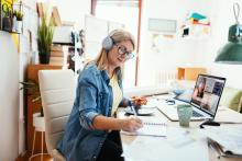 a woman sits at her desk and listents to a meeting while taking notes