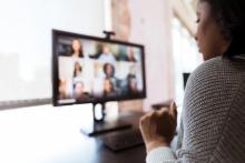 A woman looks at her computer, which has a grid of faces on it