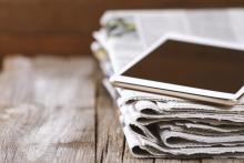 a stack of newspapers with a tablet