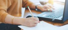 image of desk with computer with person taking notes