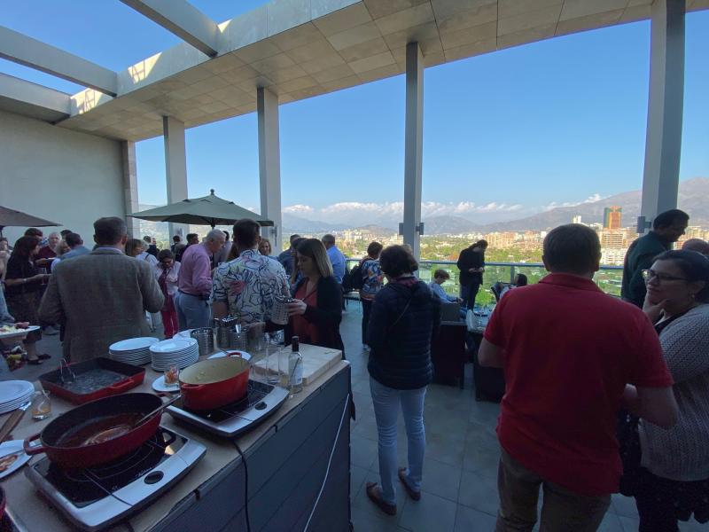 An image of a terrace looking out over Santiago, Chile. The terrace is full of people talking, and the view is sunny with blue sky and the Andes mountains in the distance