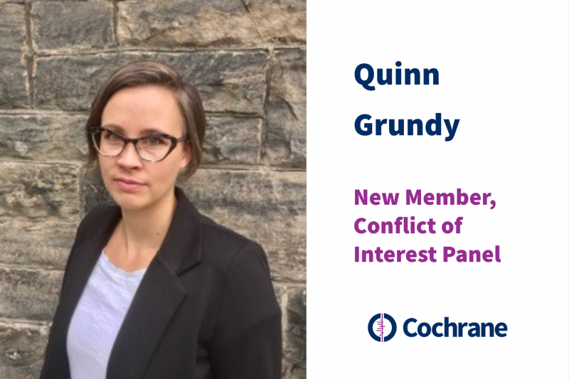 Image of Quinn Grundy, a white woman who is standing against a stone wall with a small smile and glasses